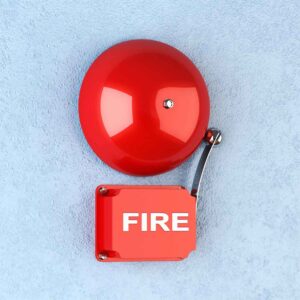Red fire alarm bell mounted on a blue wall, a key part of fire alarm design for early warning. 