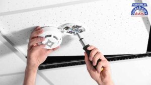 Technician installing a fire alarm system on a ceiling, ensuring proper fire alarm design and functionality.
