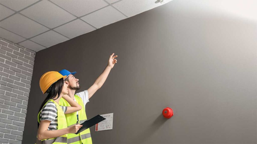 Two workers inspecting a fire alarm system in a building