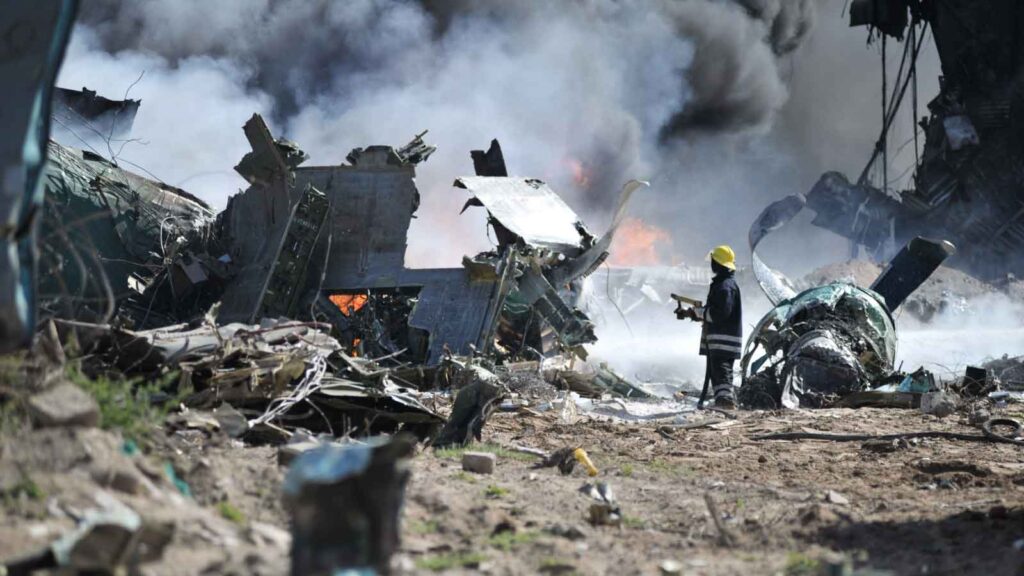 Firefighter inspects wreckage of a crashed and burning aircraft.
