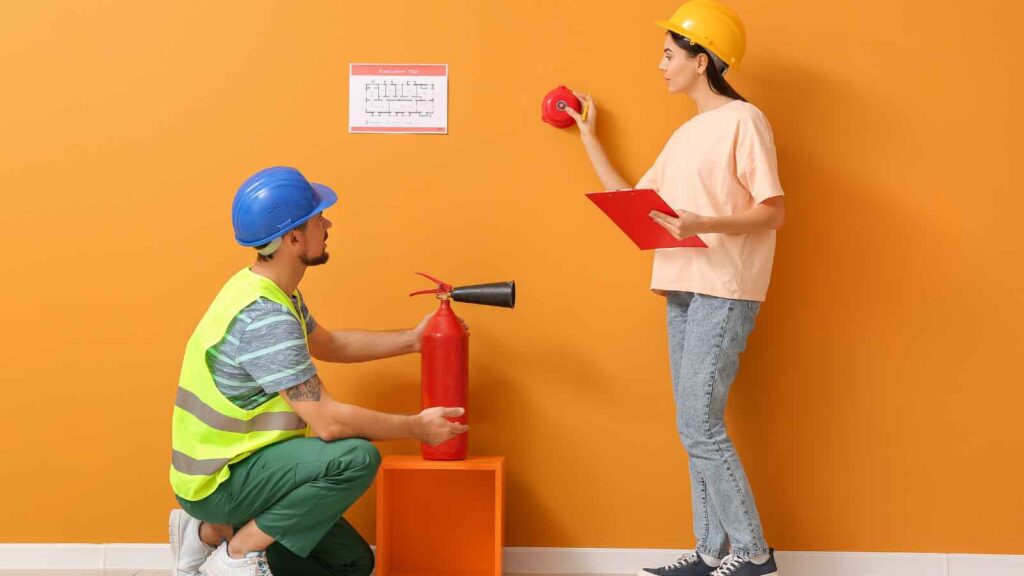 Two workers inspecting fire safety equipment and an evacuation plan.
