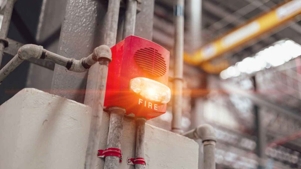 Flashing red fire alarm mounted on industrial piping.