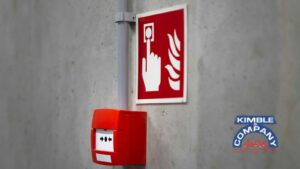 Red manual fire alarm on a concrete wall with a fire emergency sign.