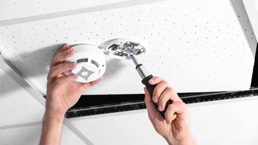 Technician installing a smoke detector on a ceiling.