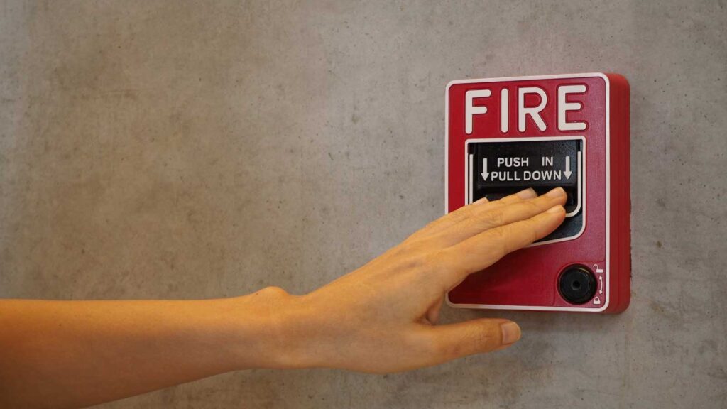 Hand reaching to pull a fire alarm.