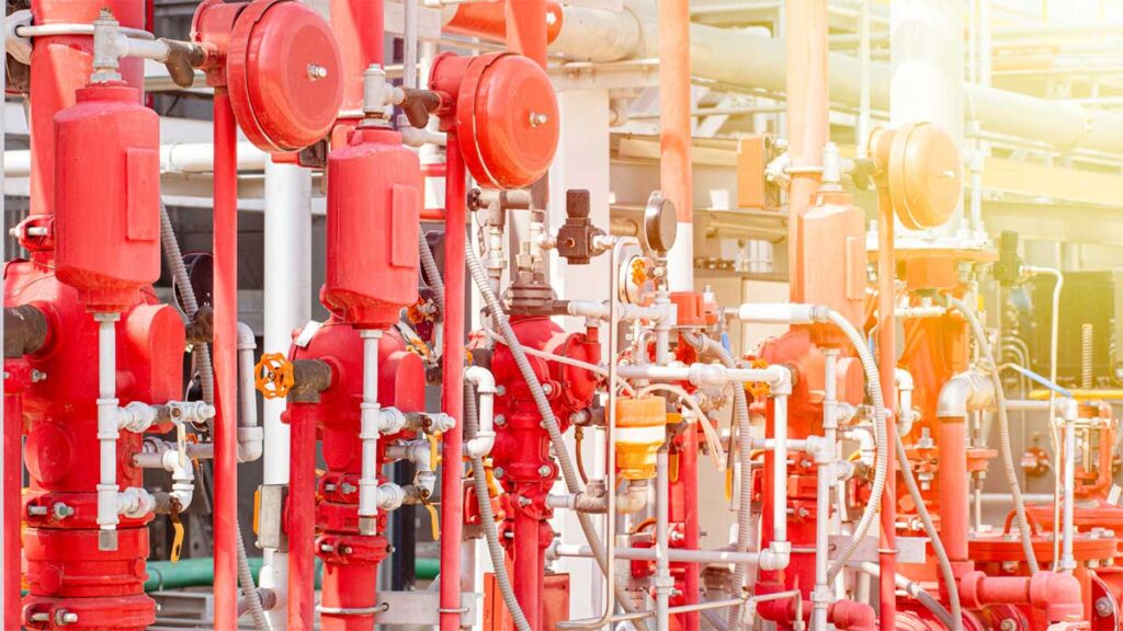Red fire sprinkler valves and pipes in an industrial area.