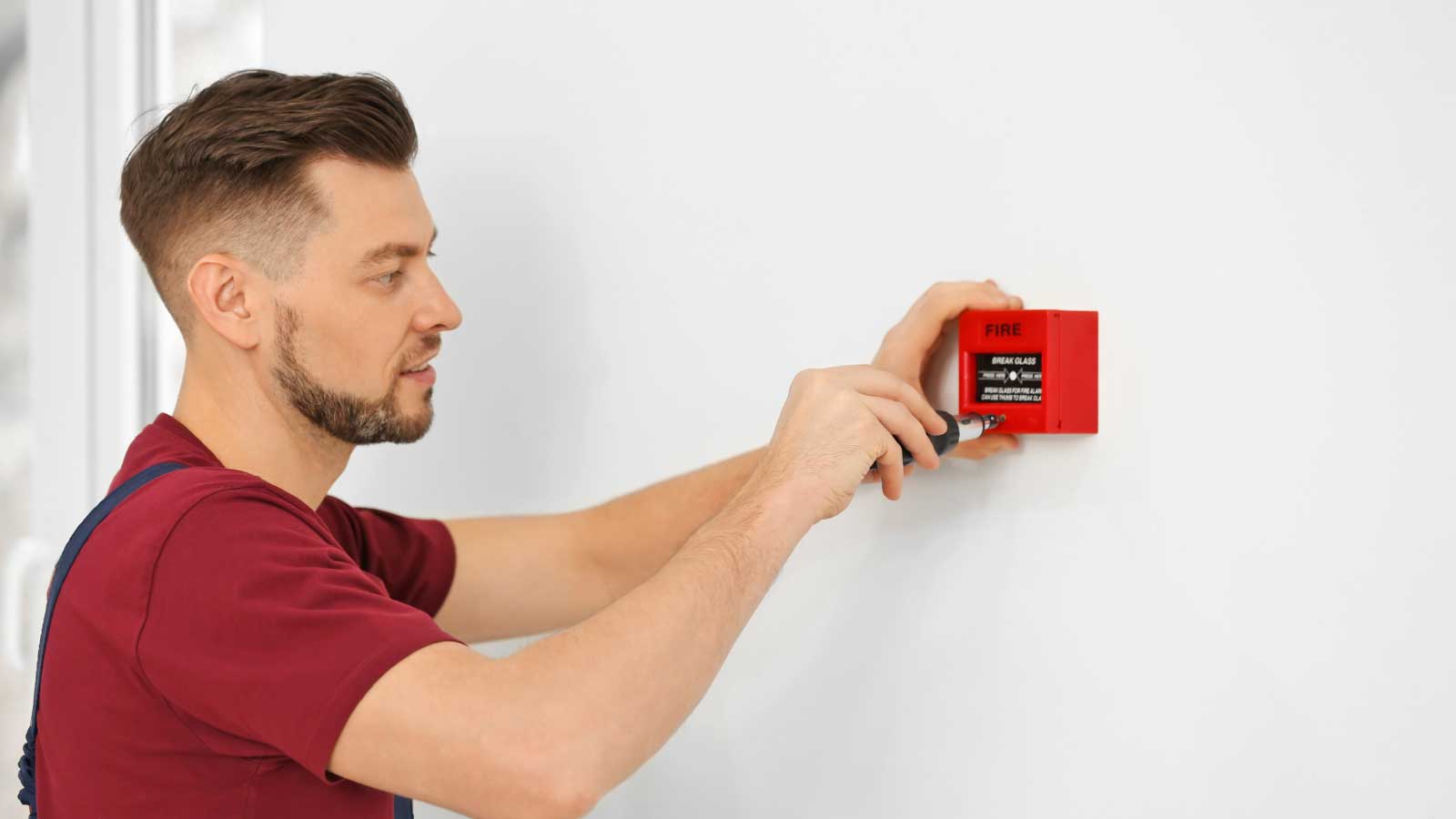 Technician installing a red fire alarm on a white wall.
