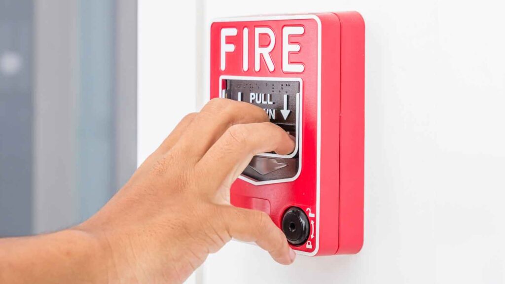 Hand pulling down a red fire alarm switch on a wall.