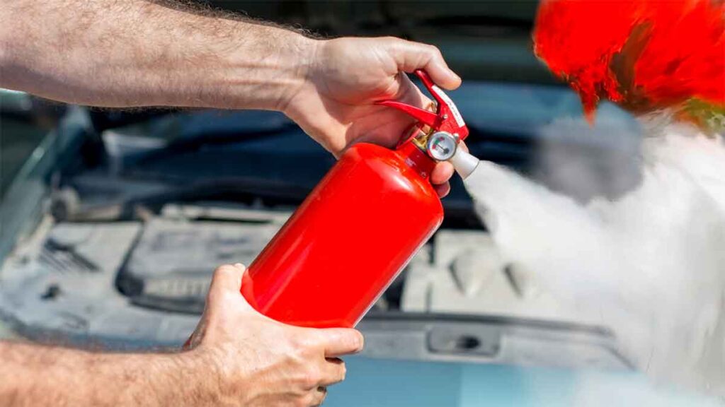 Person using a fire extinguisher on a car engine fire.