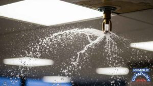Close-up of an active fire sprinkler head discharging water in a commercial building ceiling during a fire emergency.